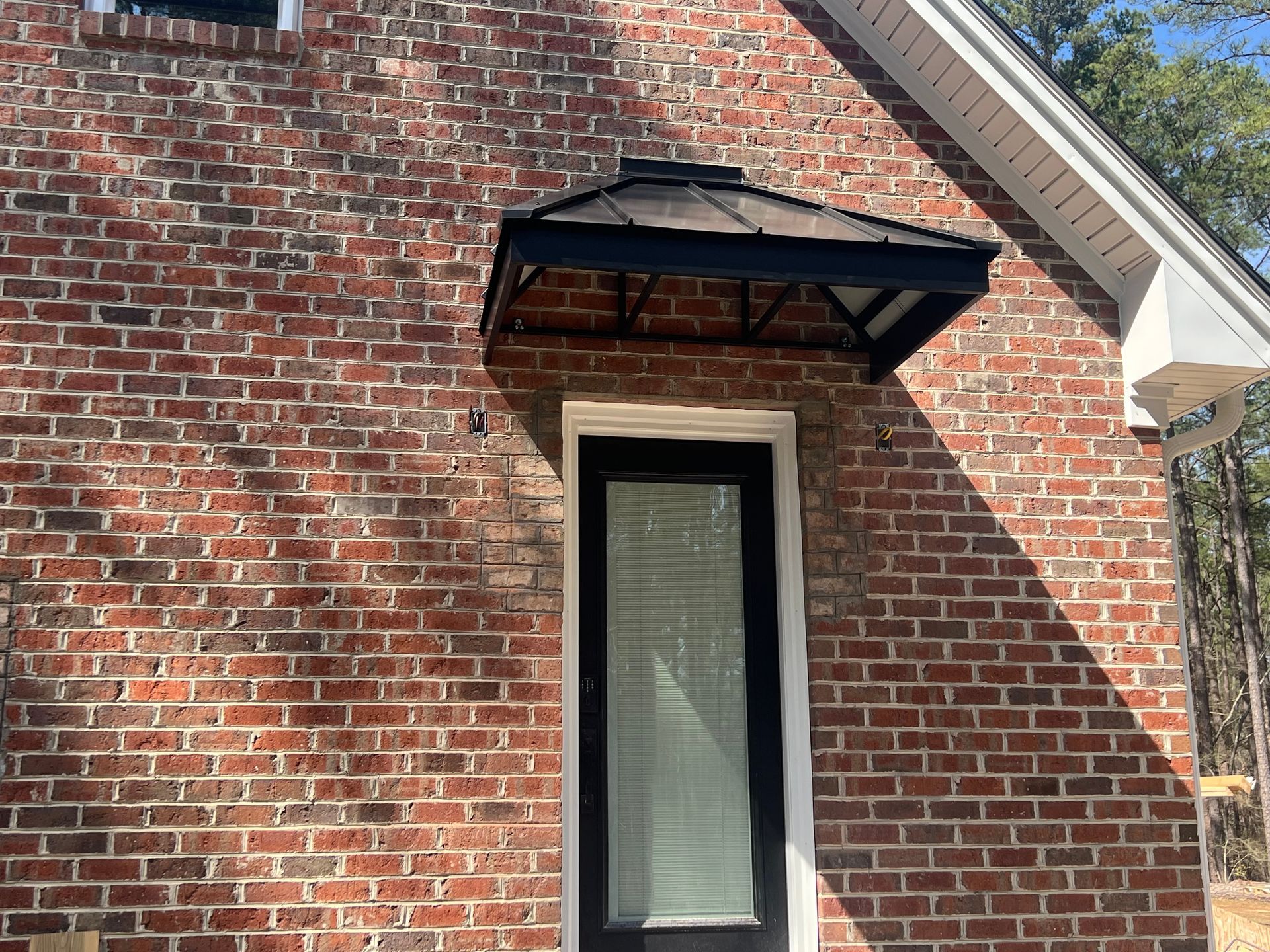 Brick exterior with a small awning above a narrow window and door frame