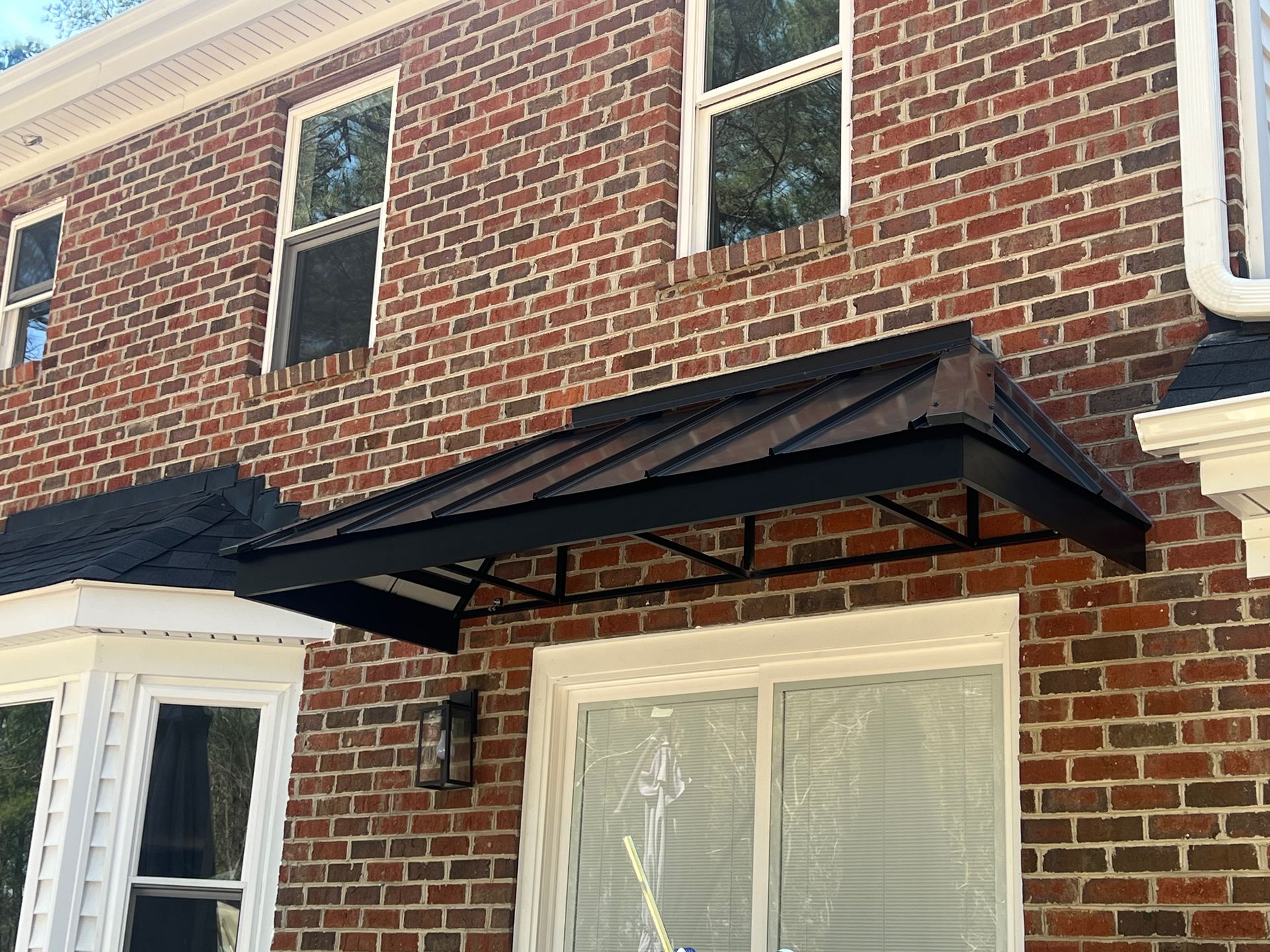 Brick house facade with black awning over a window and white-trimmed brick wall.