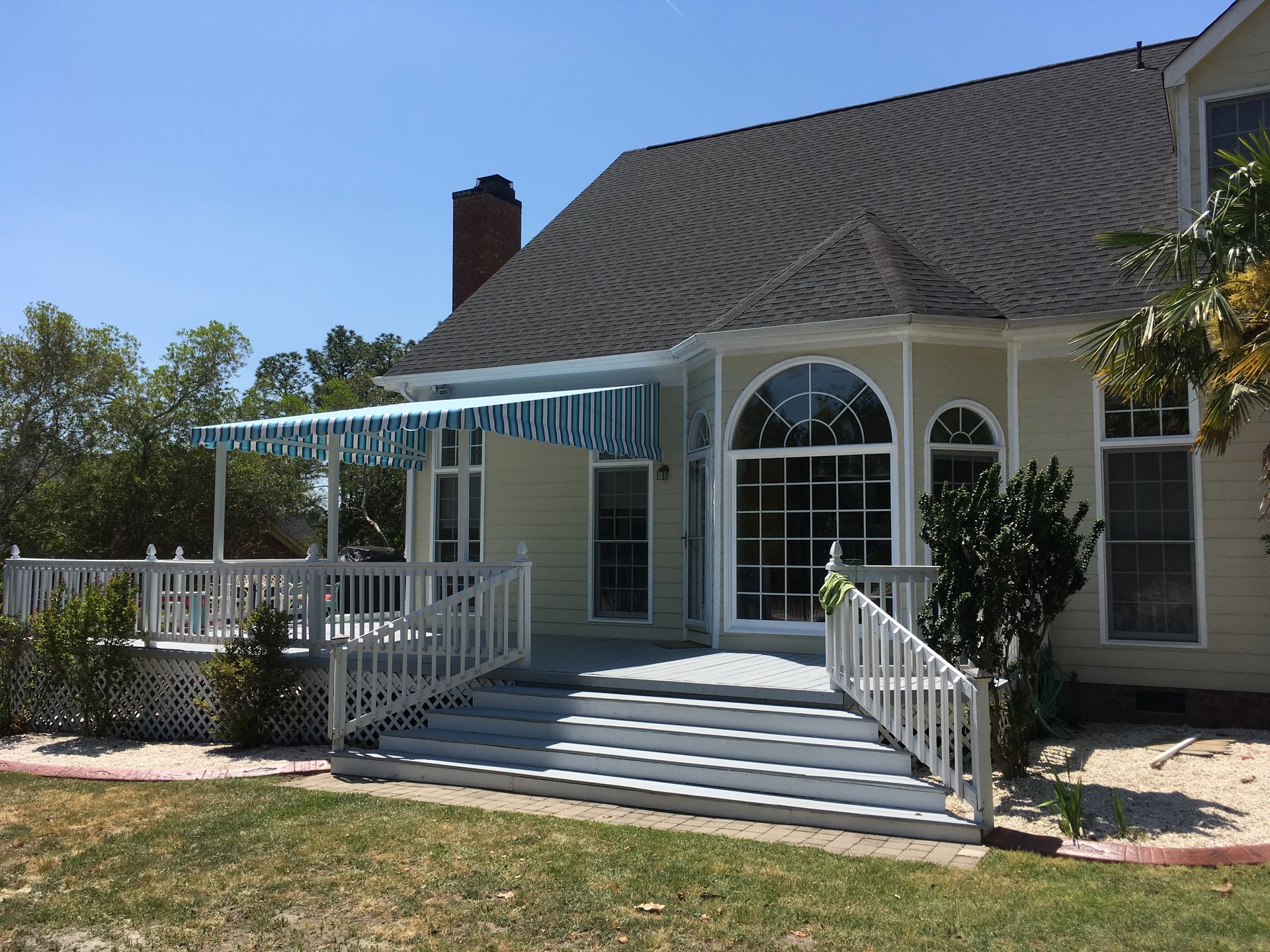 Front porch of a beige house with white railings, steps, and an arched glass door in bright sunlight