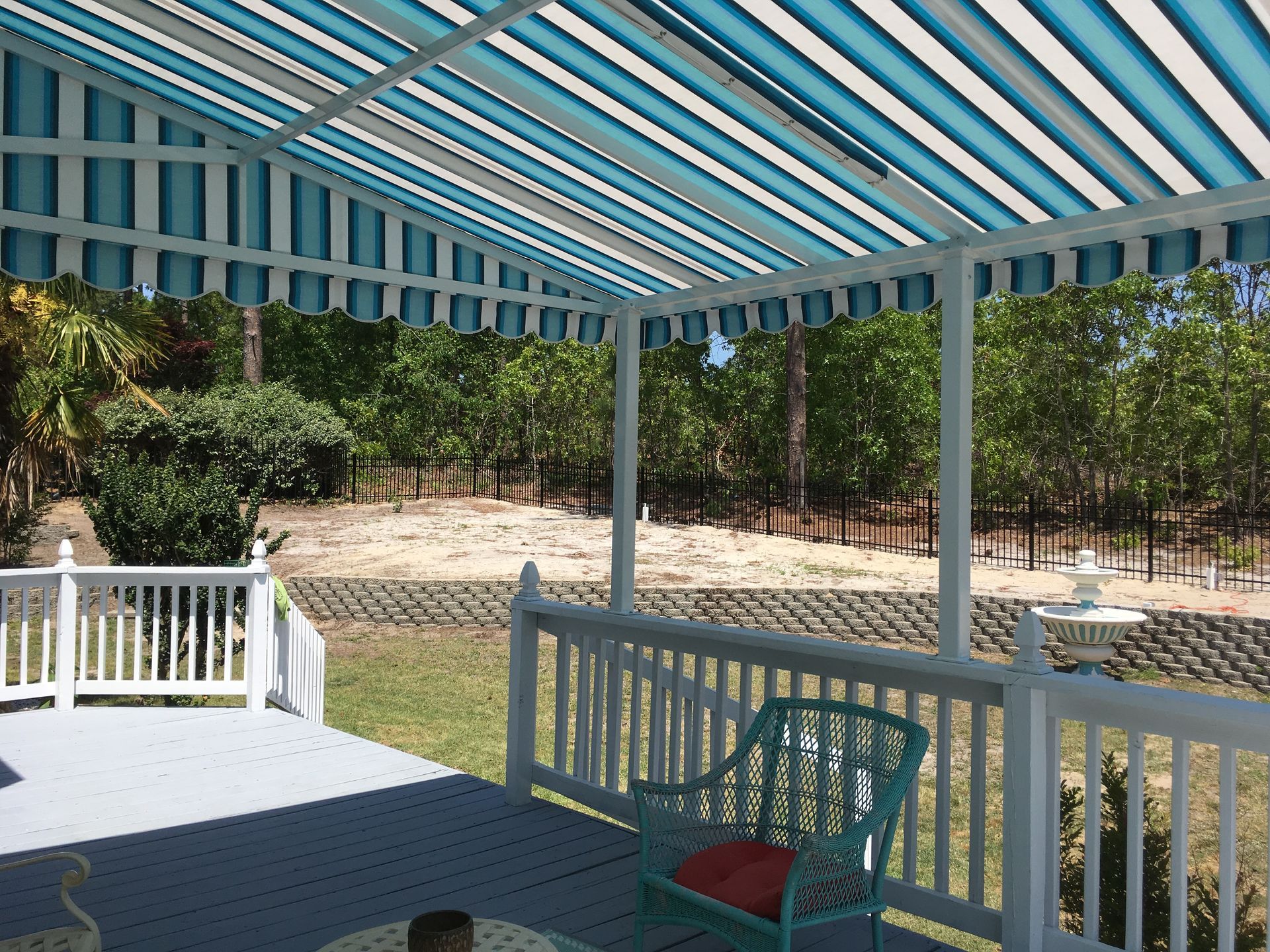 Covered porch with blue-and-white striped awning, white railing, and a wooded yard beyond.