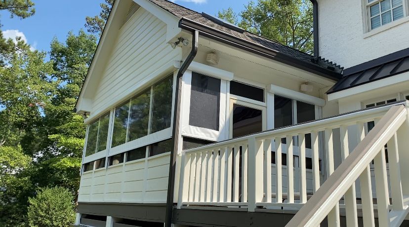 White porch with railing on a house, screened sunroom windows, and trees in the background