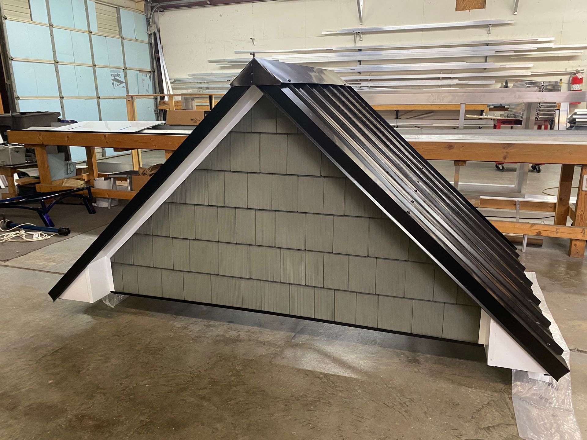 Small gray doghouse with black roof in a workshop on a concrete floor