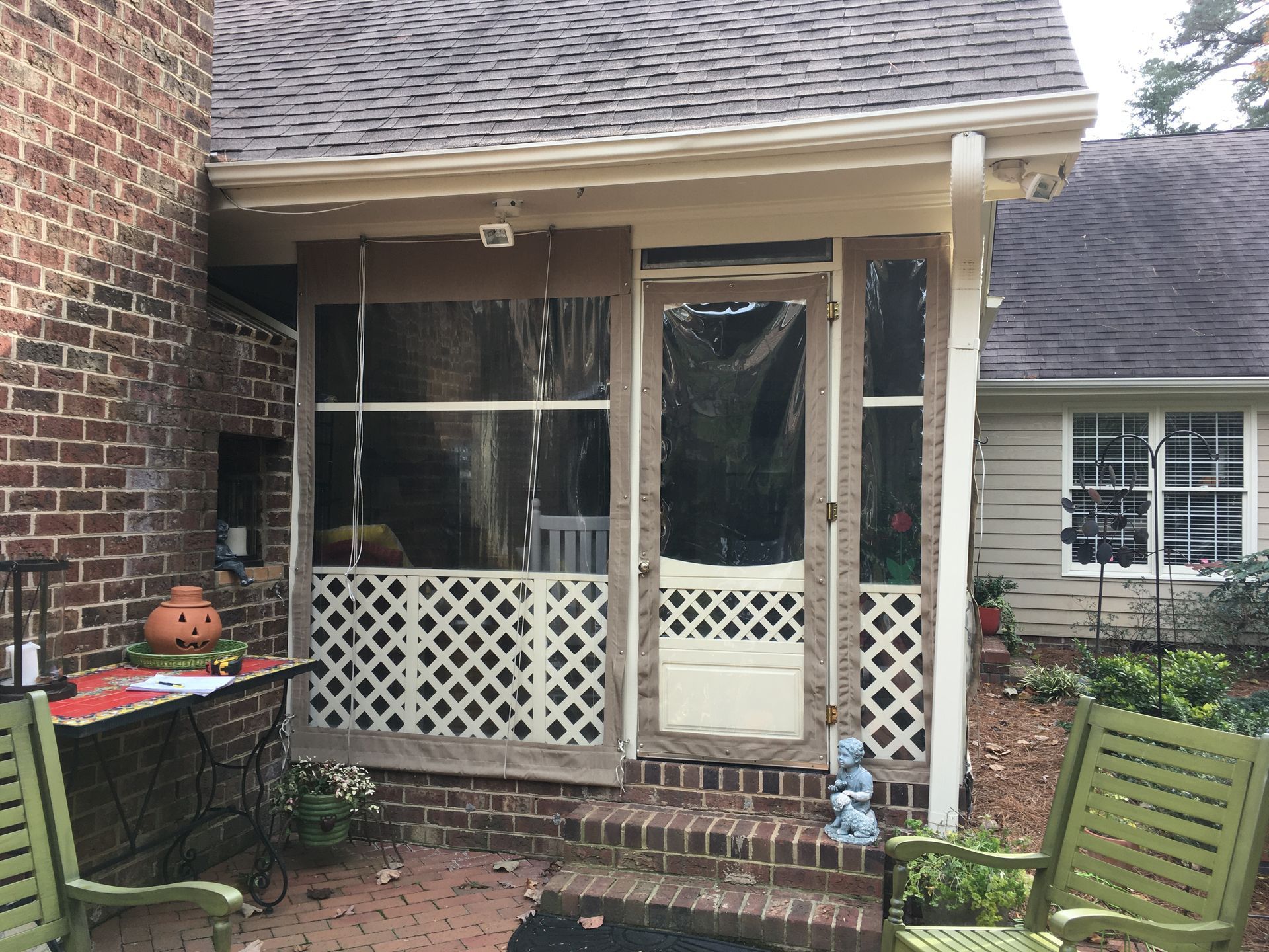 Brick patio with screened porch, white lattice railing, and two green chairs beside a brick house.