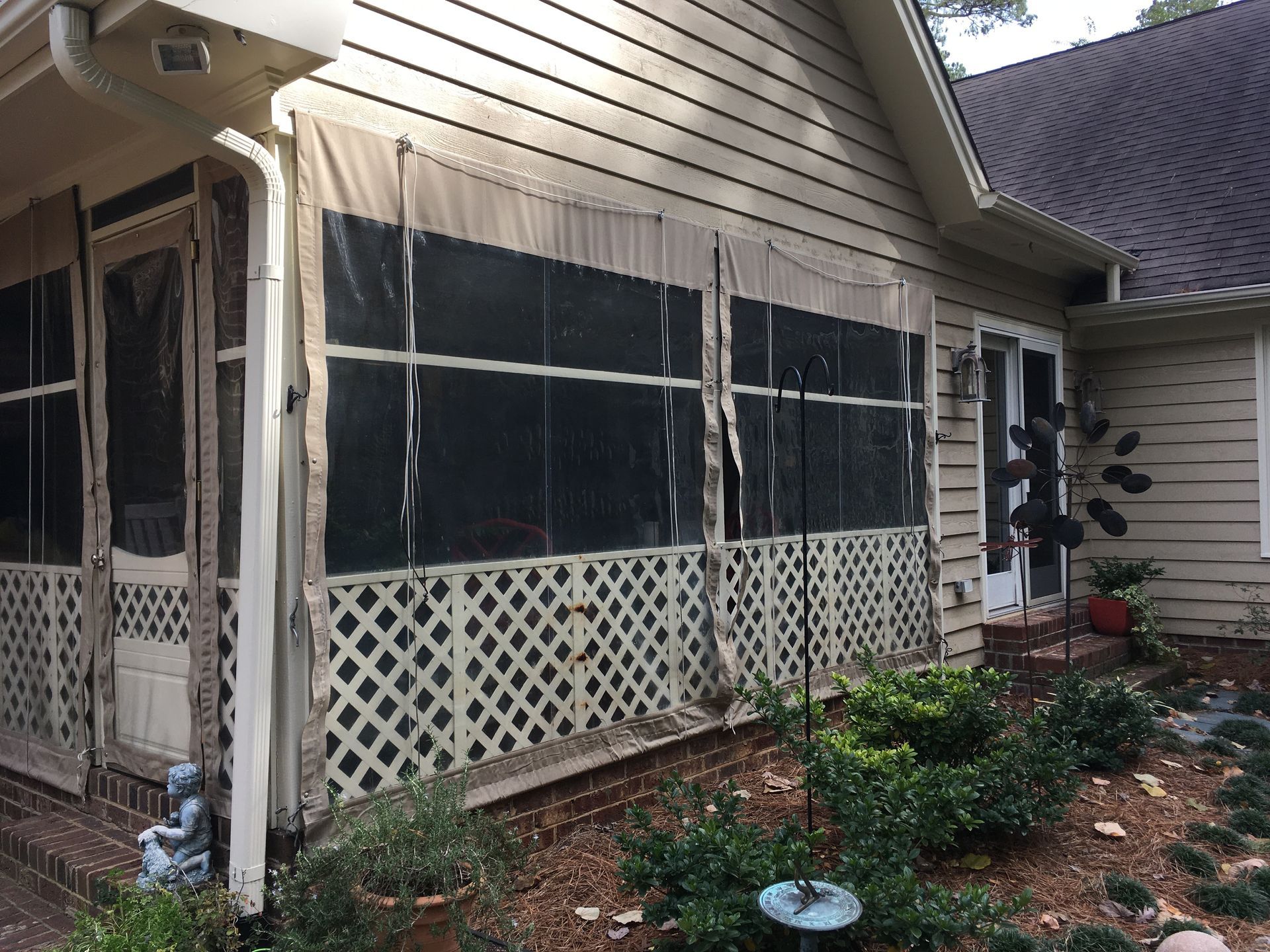 Screened porch and side yard of a beige house with lattice skirting and garden plants.