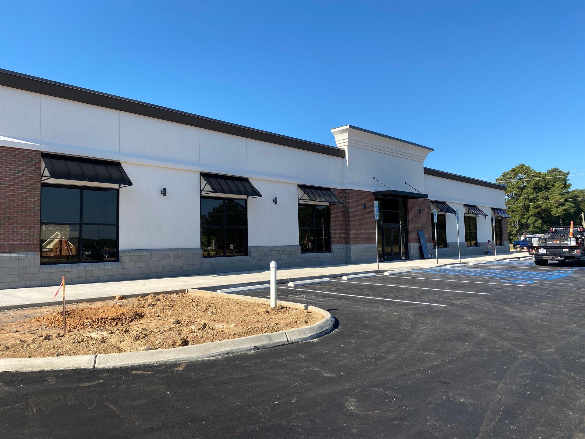 White storefront building with black awnings and a newly paved parking lot under a blue sky
