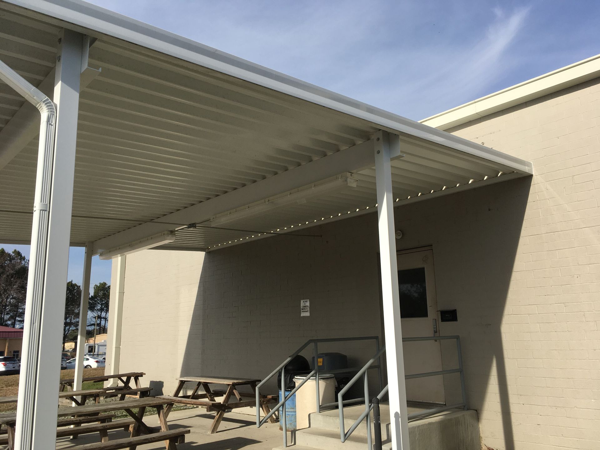 Covered outdoor patio with picnic tables beside a beige building and white support posts