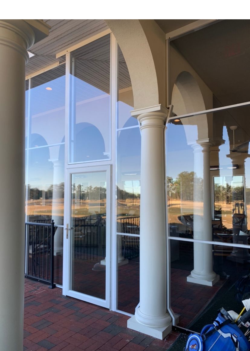 Glass storefront with white columns and arched patio, reflecting a sunny outdoor scene.
