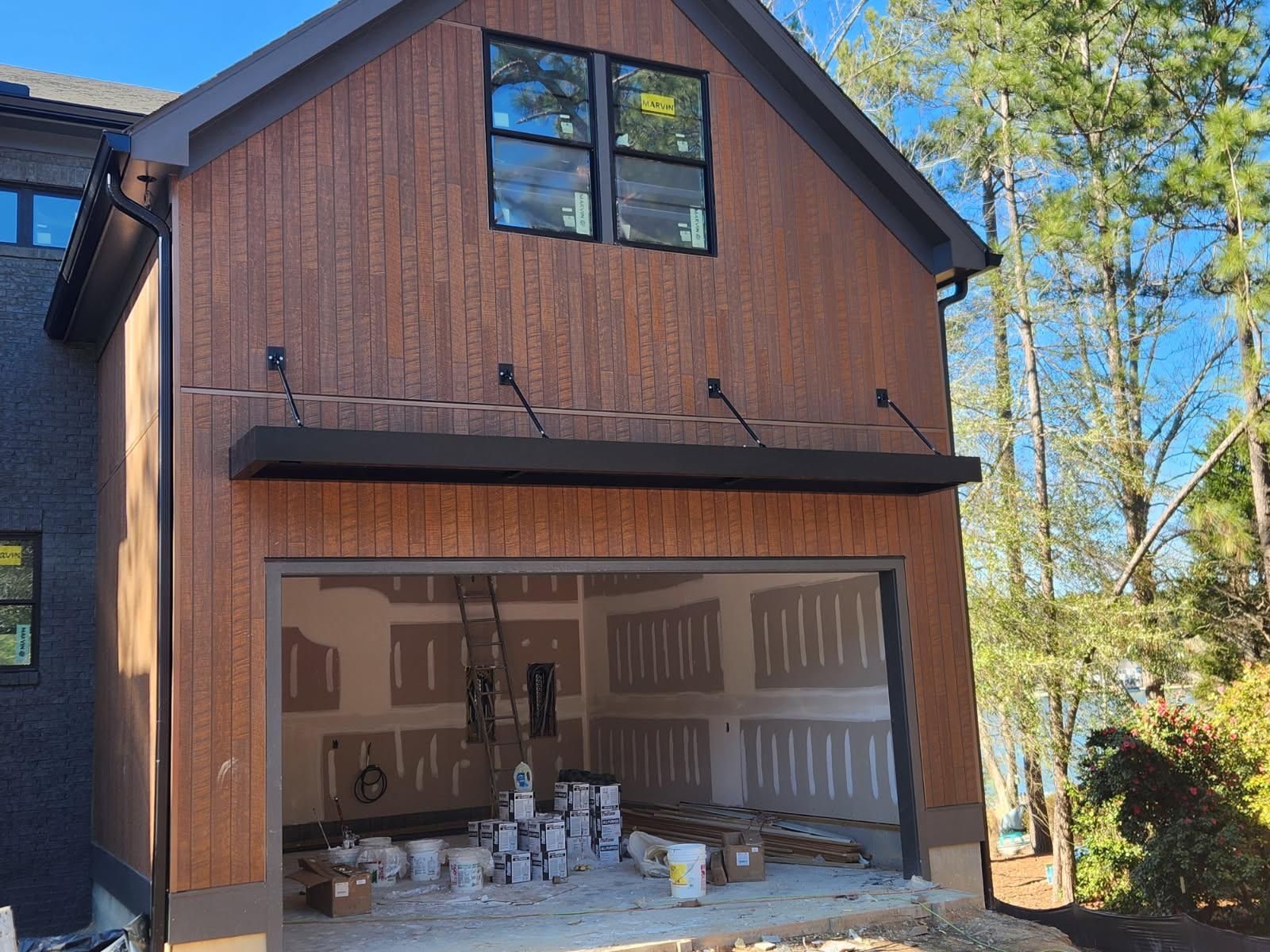 Two-story house with wood siding and an open garage under construction, tools and materials inside