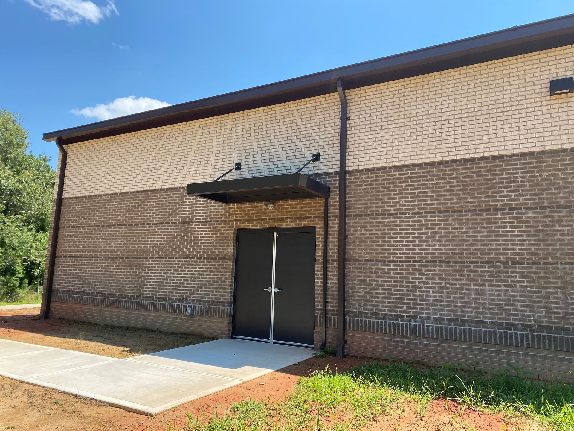 Brick building entrance with black double doors and a small awning under a blue sky