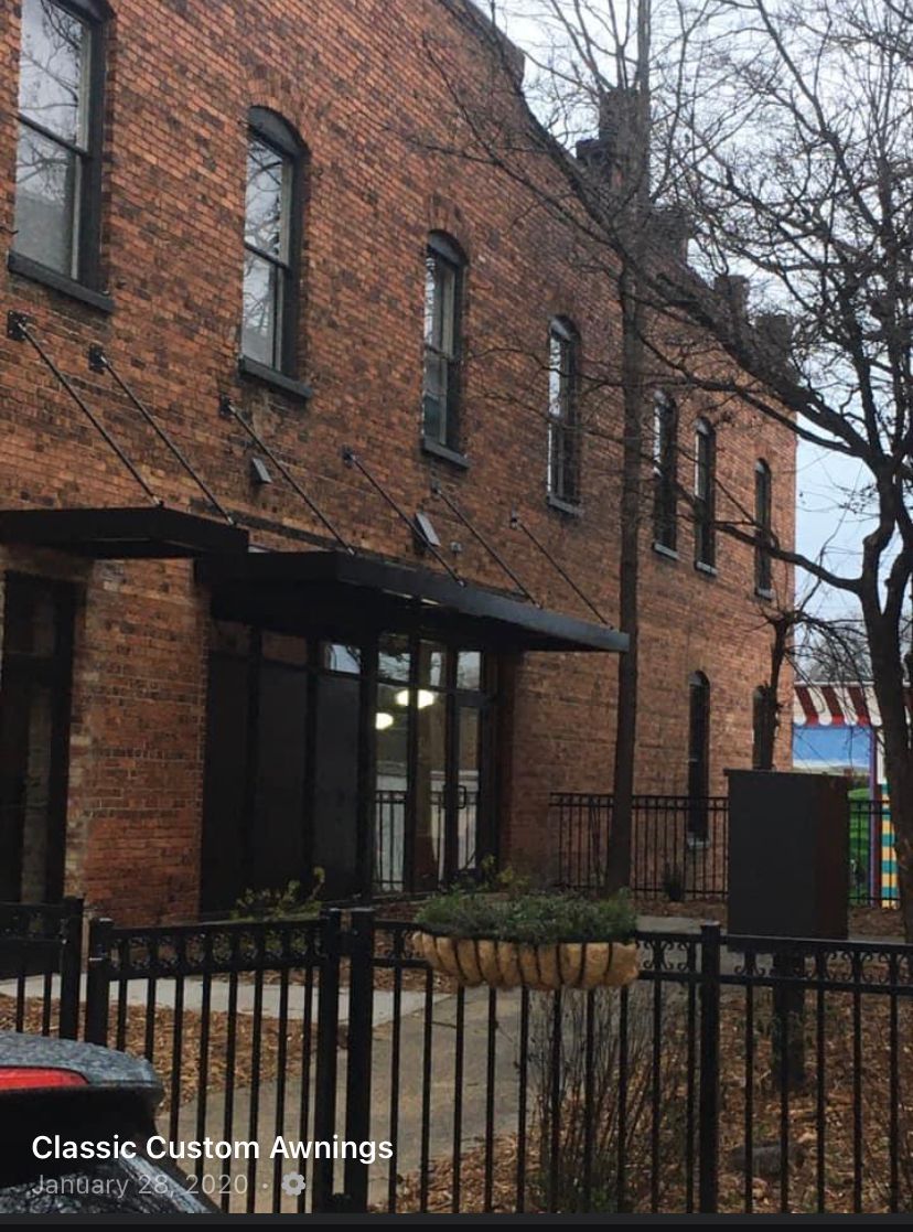Brick apartment building with black awning and wrought-iron fence along the sidewalk