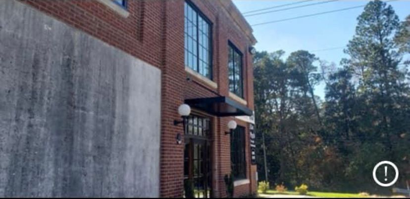 Brick building entrance with black awning and white globe light, beside trees and a concrete wall.