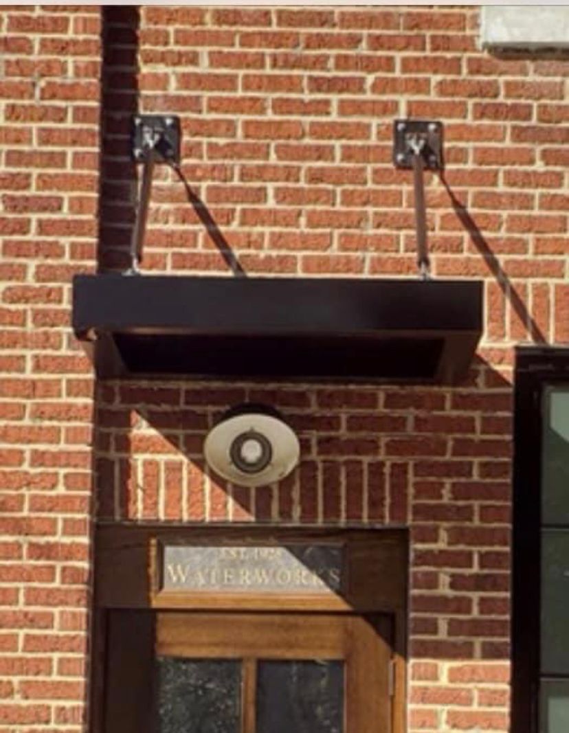 Brick building entrance with a black awning, round wall light, and wooden door