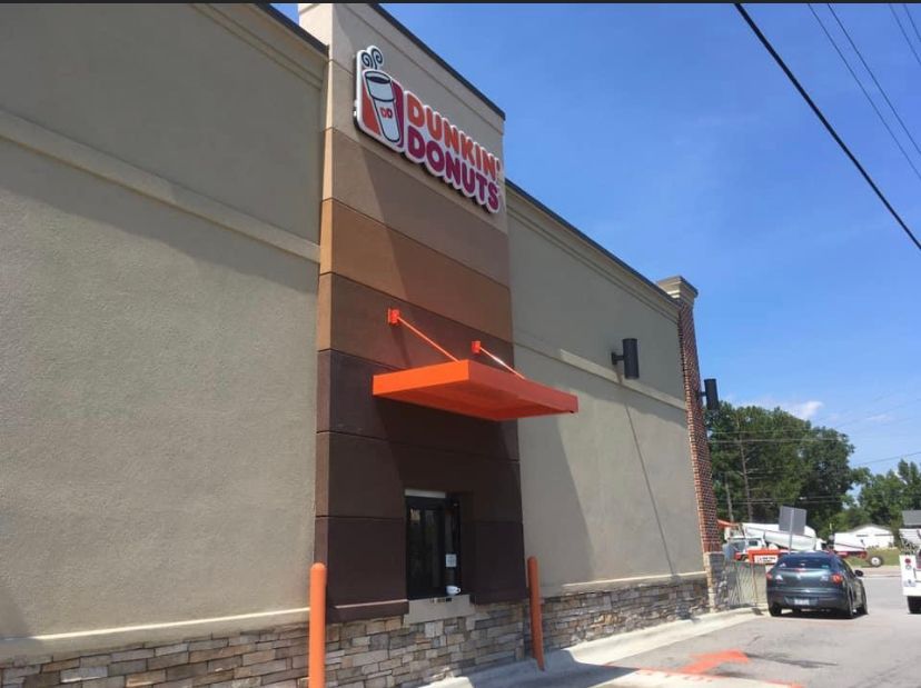 Dunkin’ storefront with orange awning and parked cars outside on a sunny day