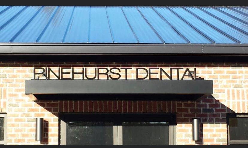 Brick building with blue roof and sign reading “BINEHURST DENTAL” above the entrance