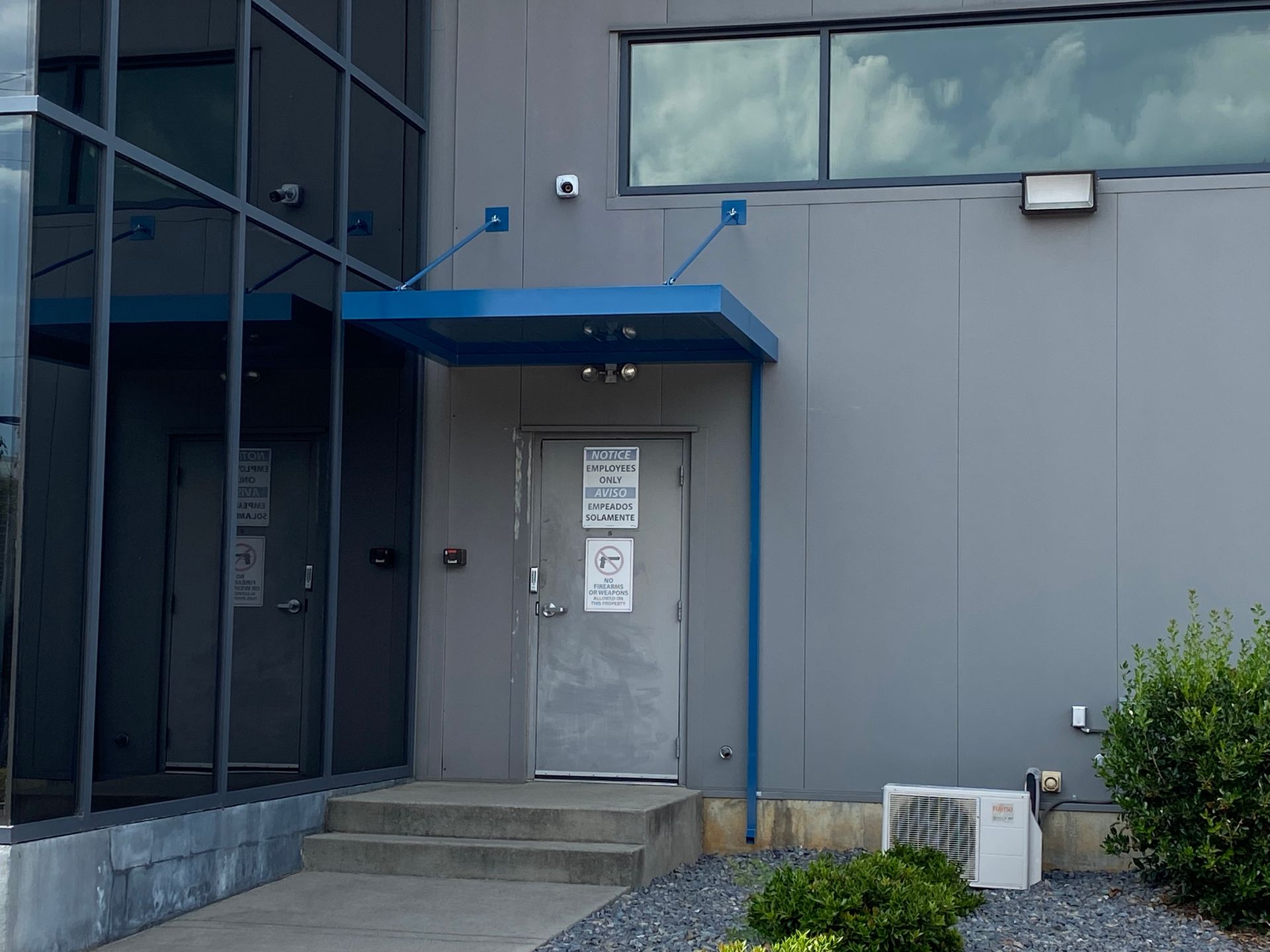 Building entrance with blue awning, gray door, and steps beside glass windows.