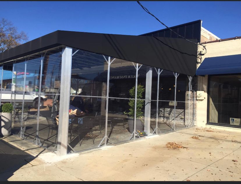 Outdoor patio with clear plastic walls and black canopy outside a building