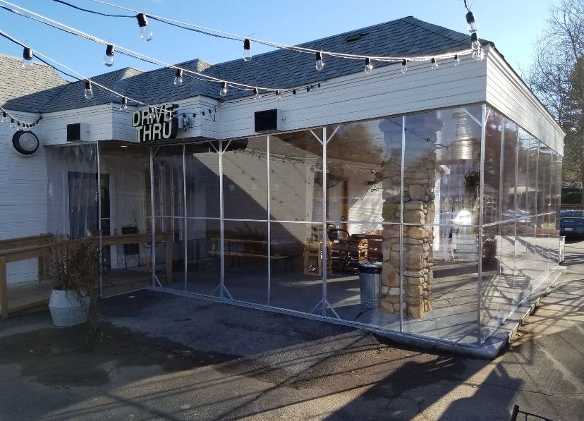 Clear plastic enclosure around a storefront patio with string lights and potted plants in winter sunlight