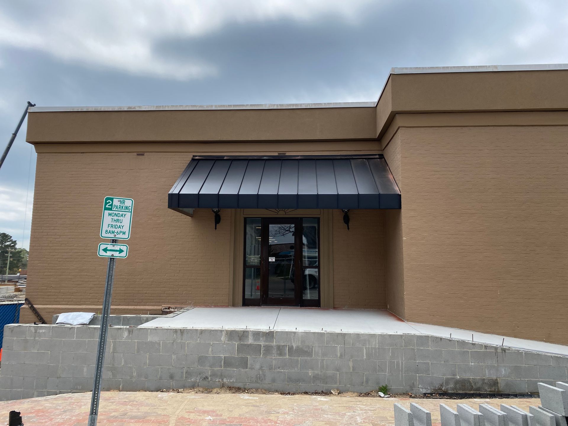 Small brick building entrance with black awning and concrete ramp under cloudy sky