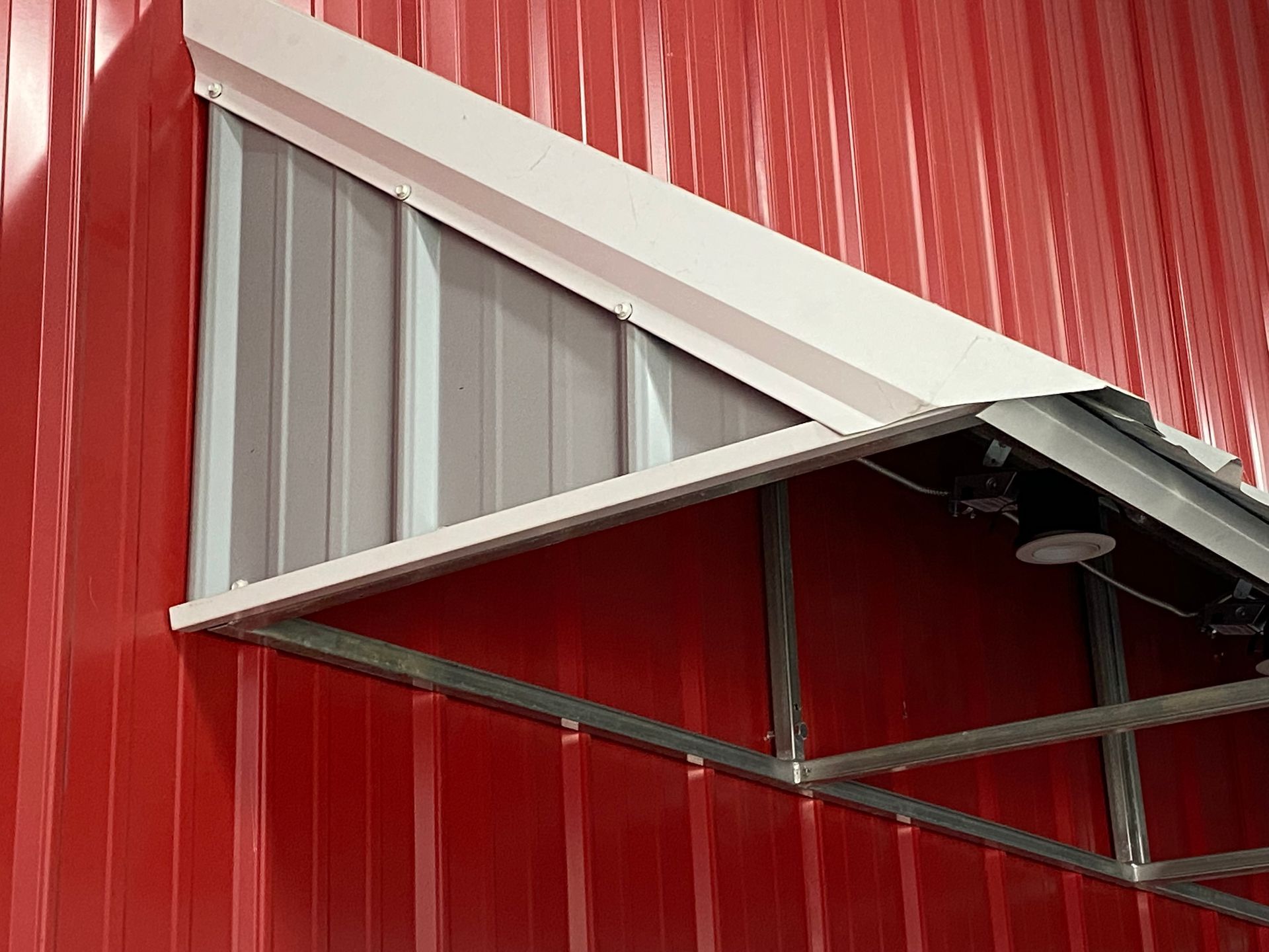 Red metal building wall with a small triangular awning and window frame.