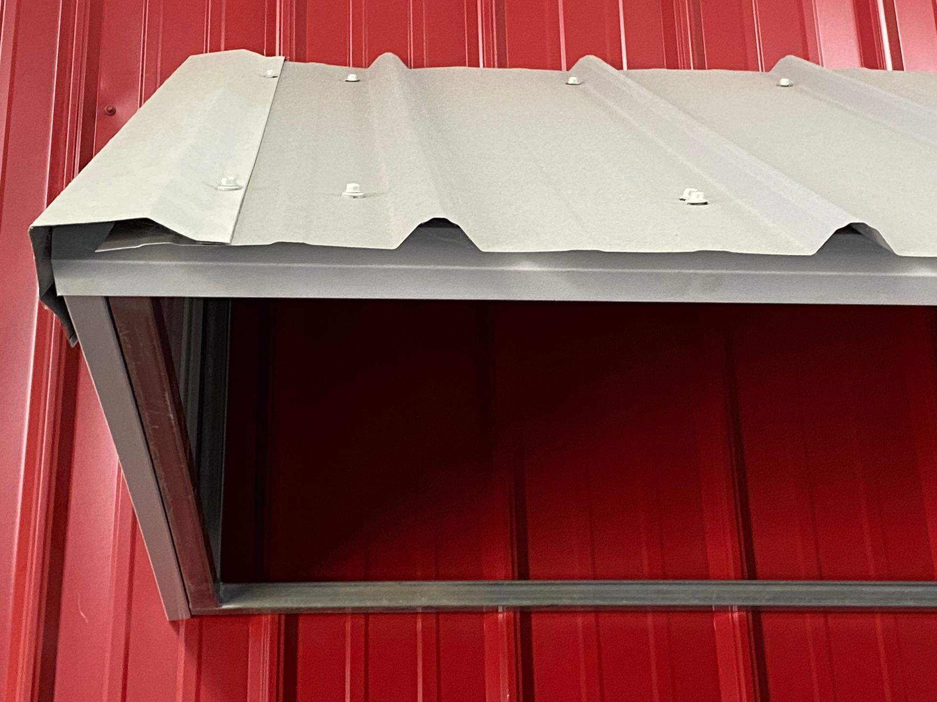 Small gray corrugated metal awning attached to a red wall, viewed from below