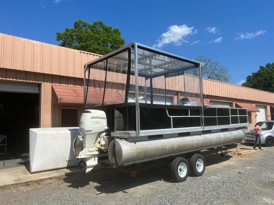Pontoon boat on a trailer beside a building, with a black metal canopy frame.