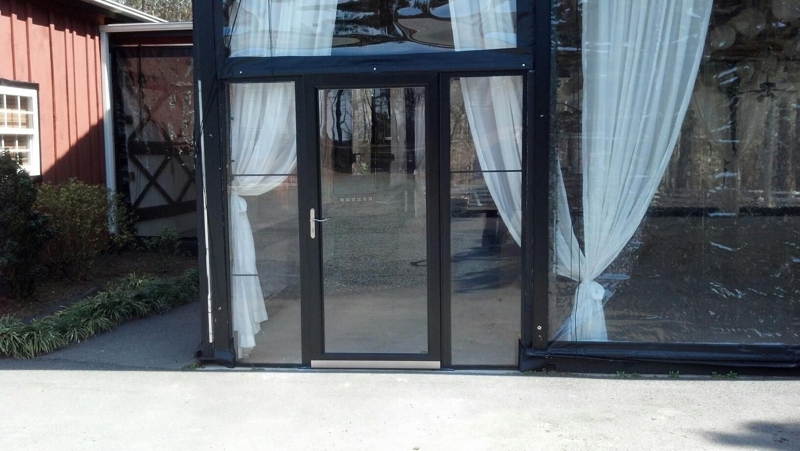 Glass entrance doors with black frames and white curtains in front of a building