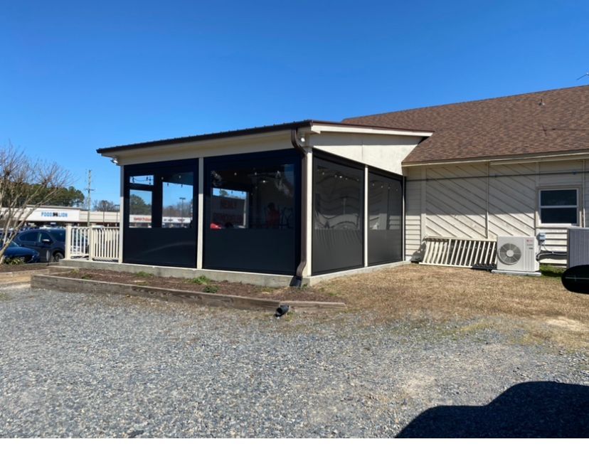Small covered porch with dark siding on a building, gravel foreground, and a clear blue sky.