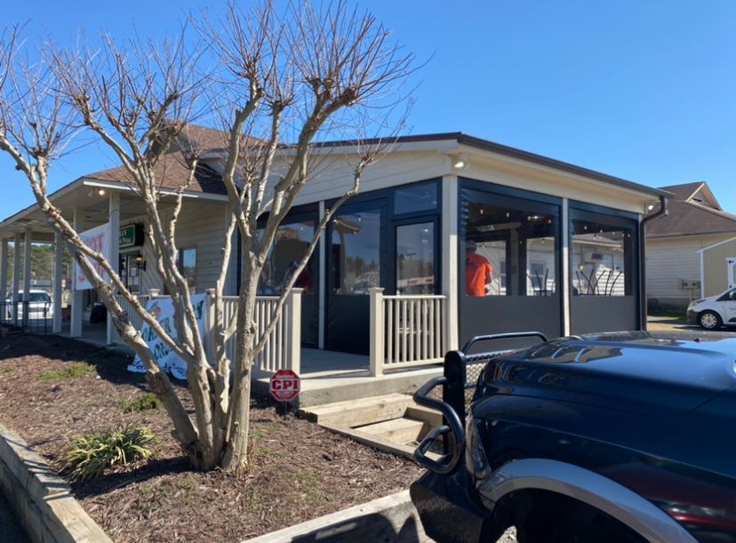 House exterior with enclosed porch, leafless tree, and a black vehicle in the driveway under a clear blue sky