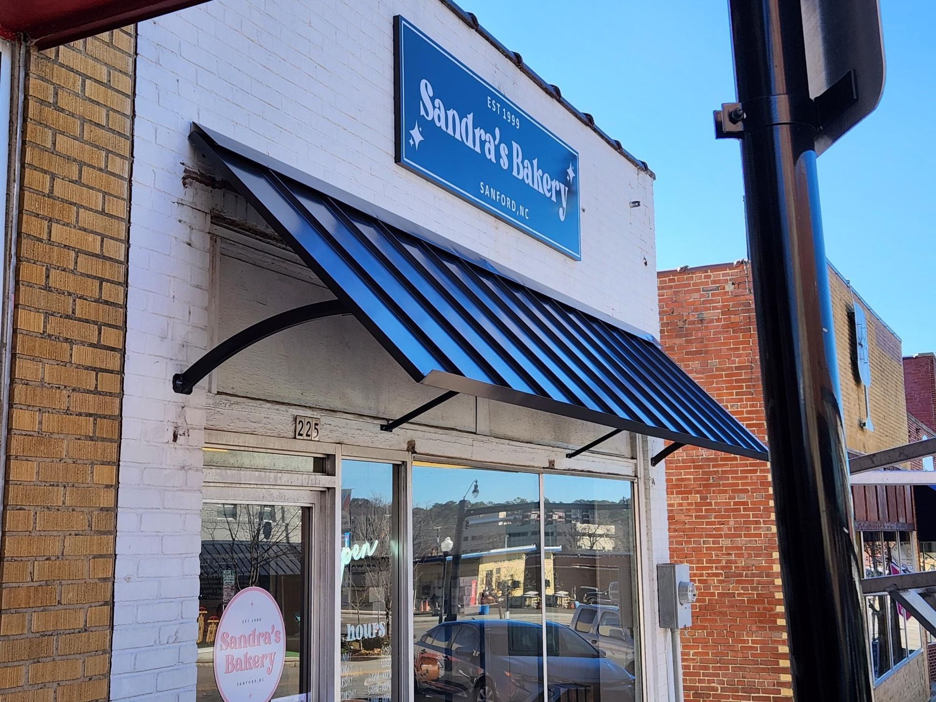 Storefront with blue-and-white striped awning and sign above the entrance on a sunny street.