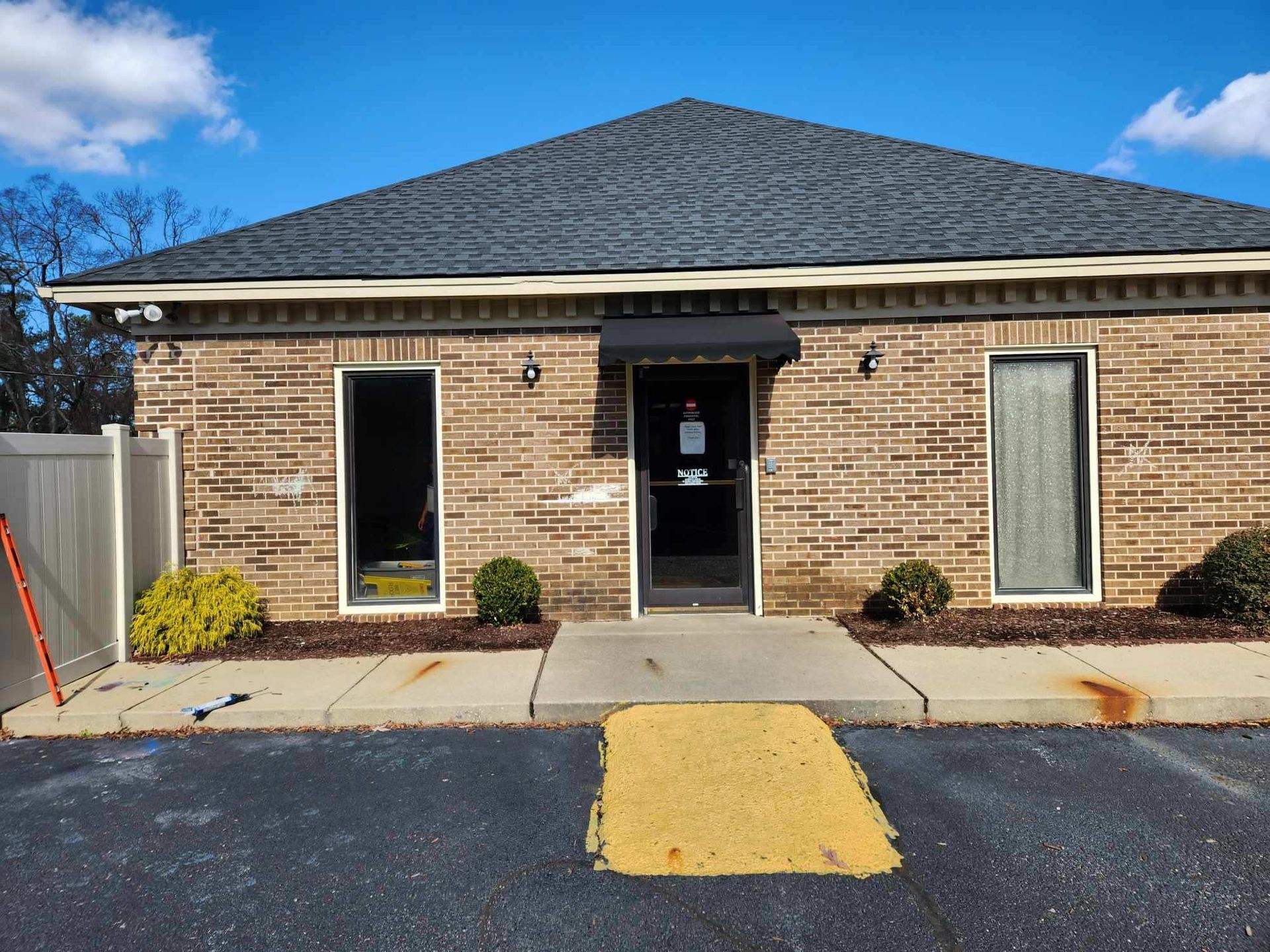 Brick building entrance with central door, two windows, and a yellow curb ramp in front