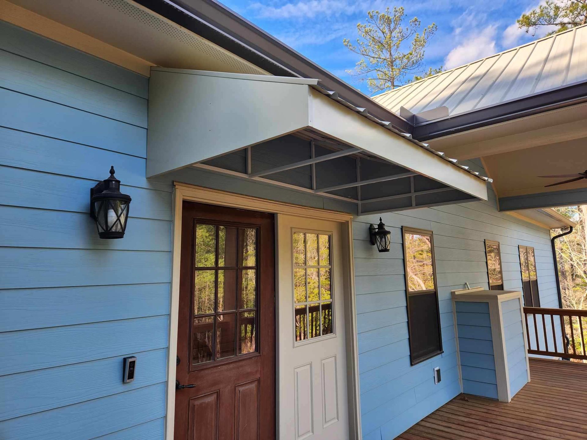Blue house exterior with wood front doors, porch light, and white trim under a sunny sky