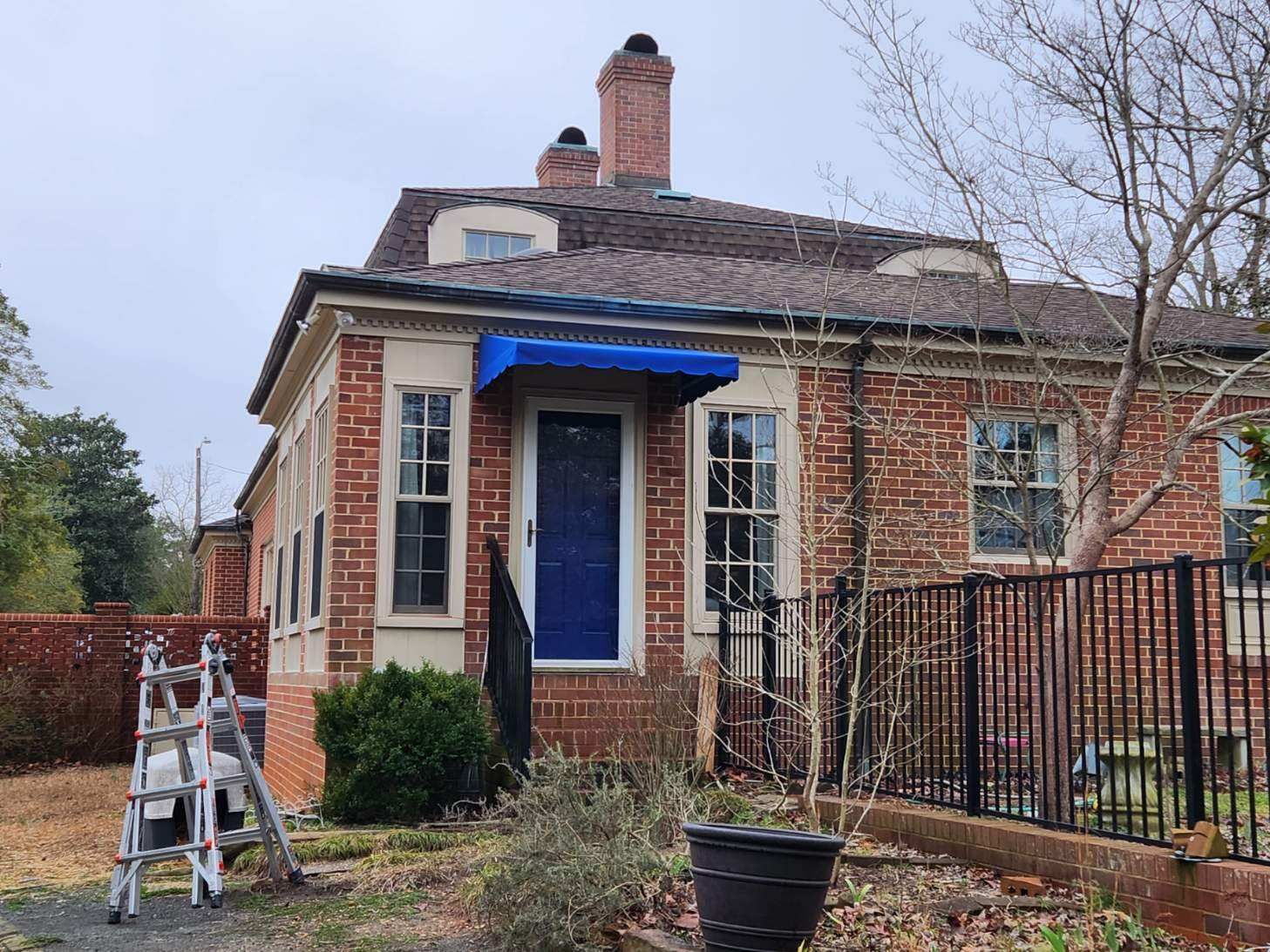 Brick house exterior with blue awning over the front door and a ladder in the yard