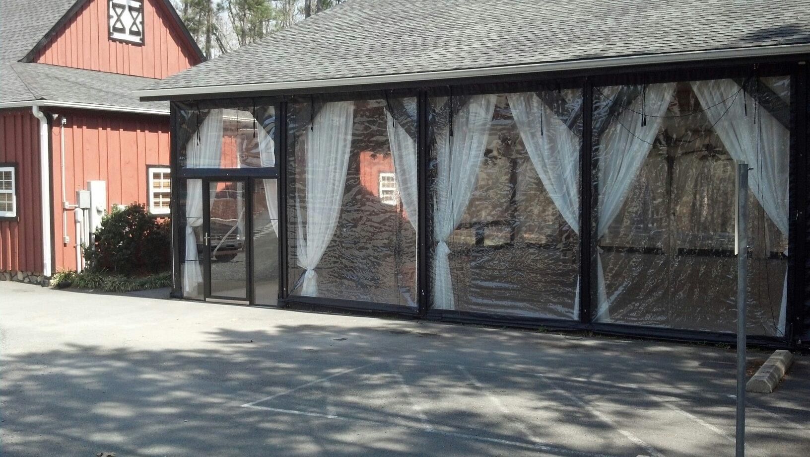Outdoor barn-style building with white curtains over large windows and a small glass entryway in front