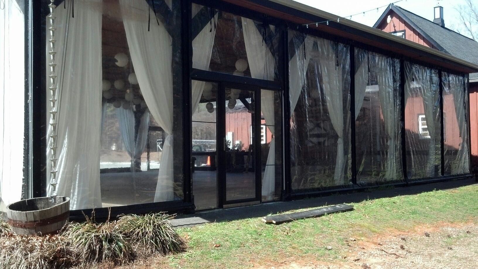 Modern glass patio room with sheer curtains and a red-roofed house in the background