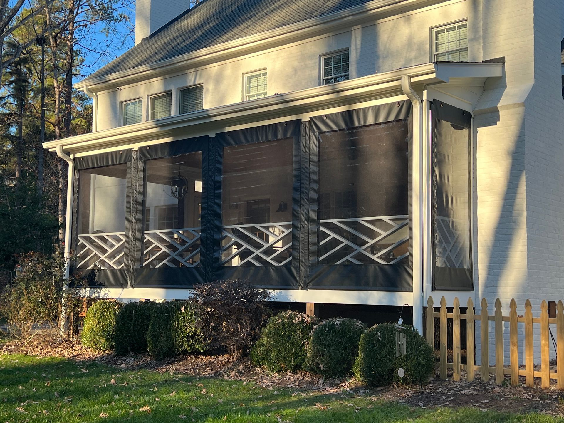 Front porch of a cream house with dark screened panels, striped awning, and a small white picket fence