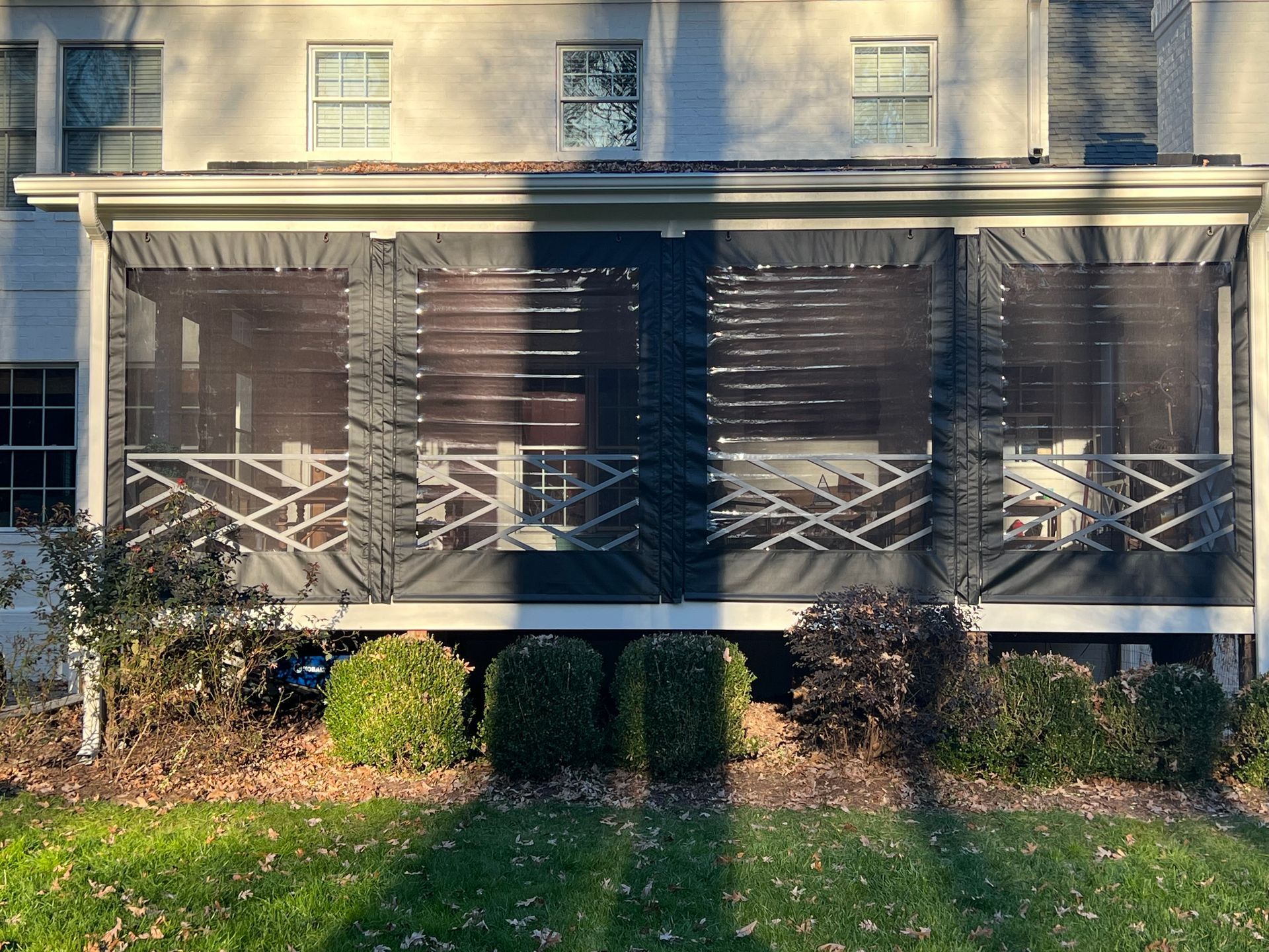 Screened porch on a beige house with white railings and shrubs in front, lit by long shadows.