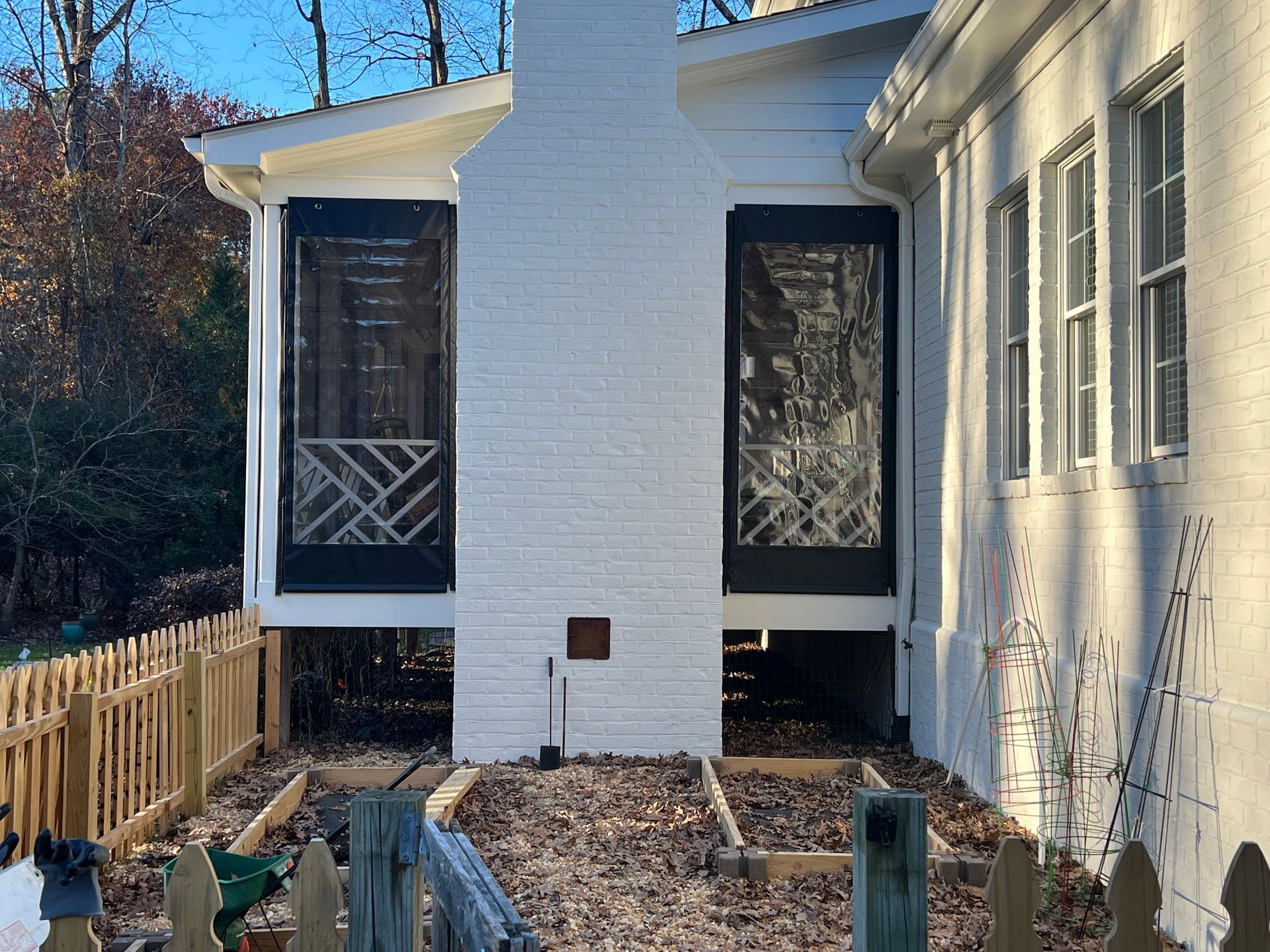 Backyard side of a white house with a small porch, fence, and leaf-covered ground under a clear blue sky