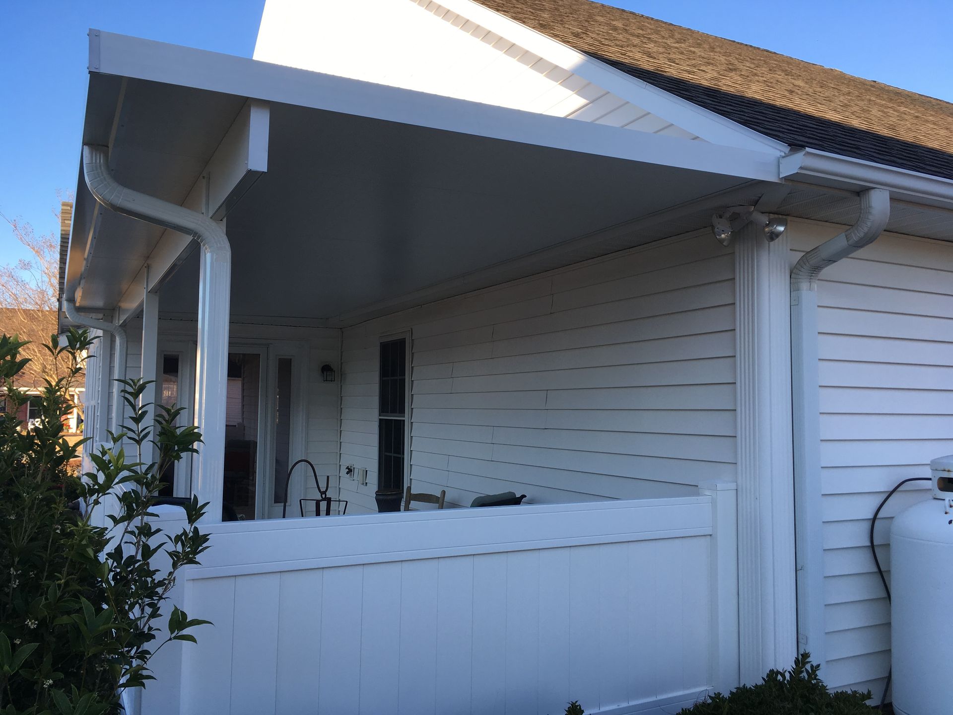 White porch with railing and posts on a house exterior under a sloped roof.