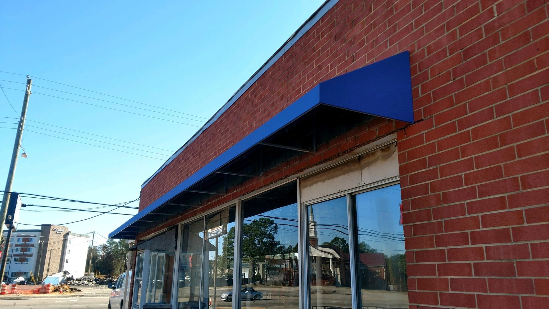 Storefront with blue awning and red brick facade along a sunny street