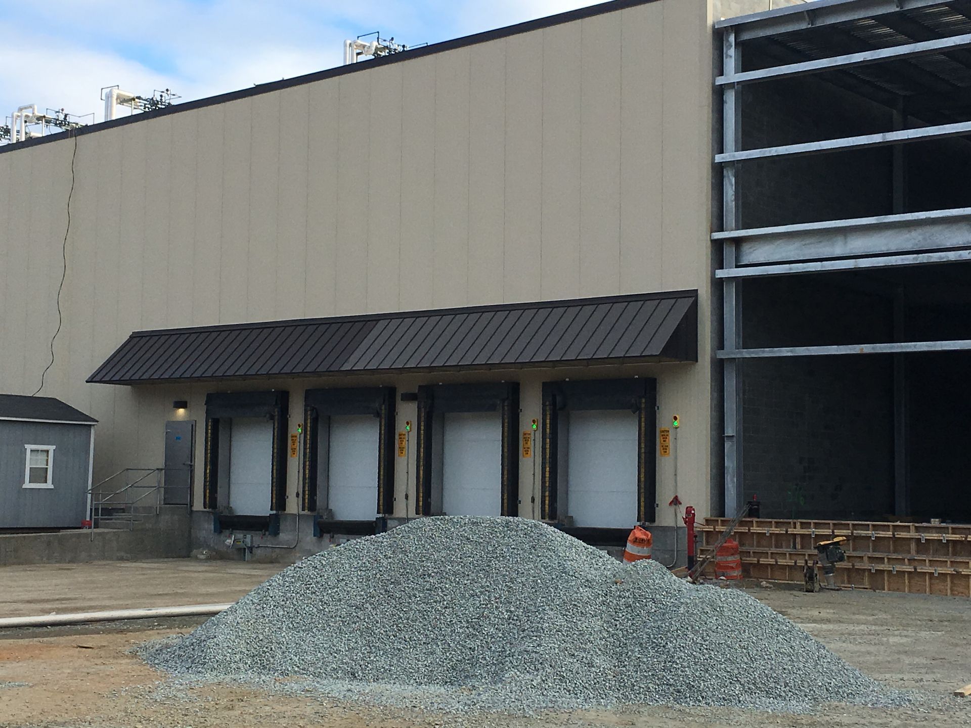 Construction site with gravel pile, loading docks, and a large industrial building wall