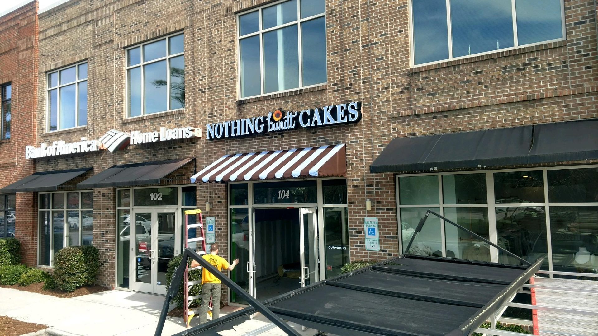 Brick storefronts with striped awning; cake shop sign and black pickup truck in front.