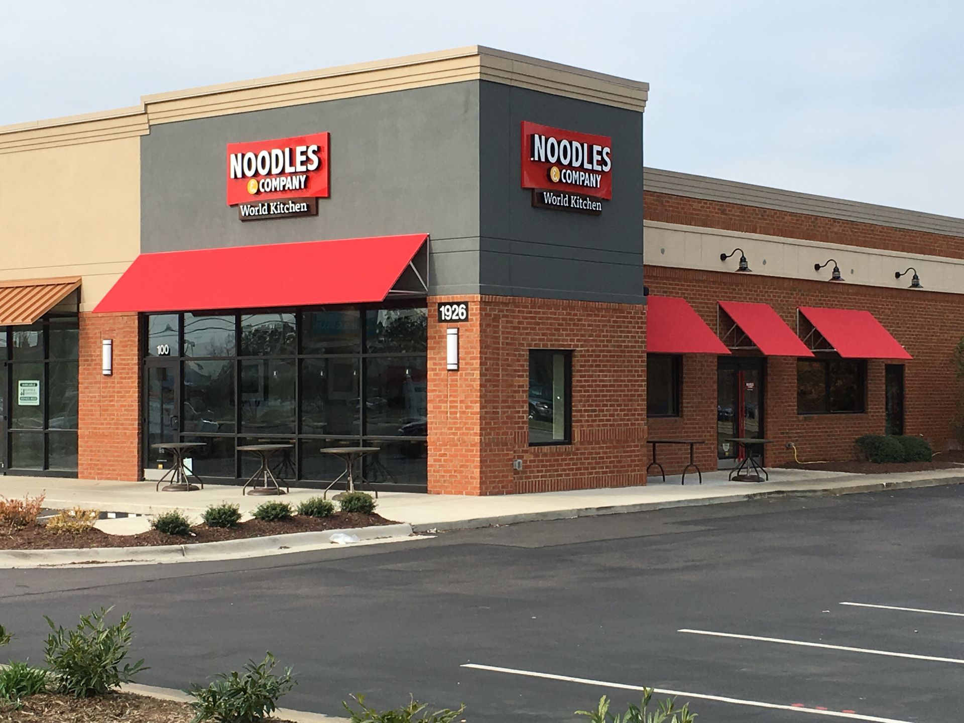 Noodles & Company restaurant exterior with red awnings and beige brick facade in a parking lot