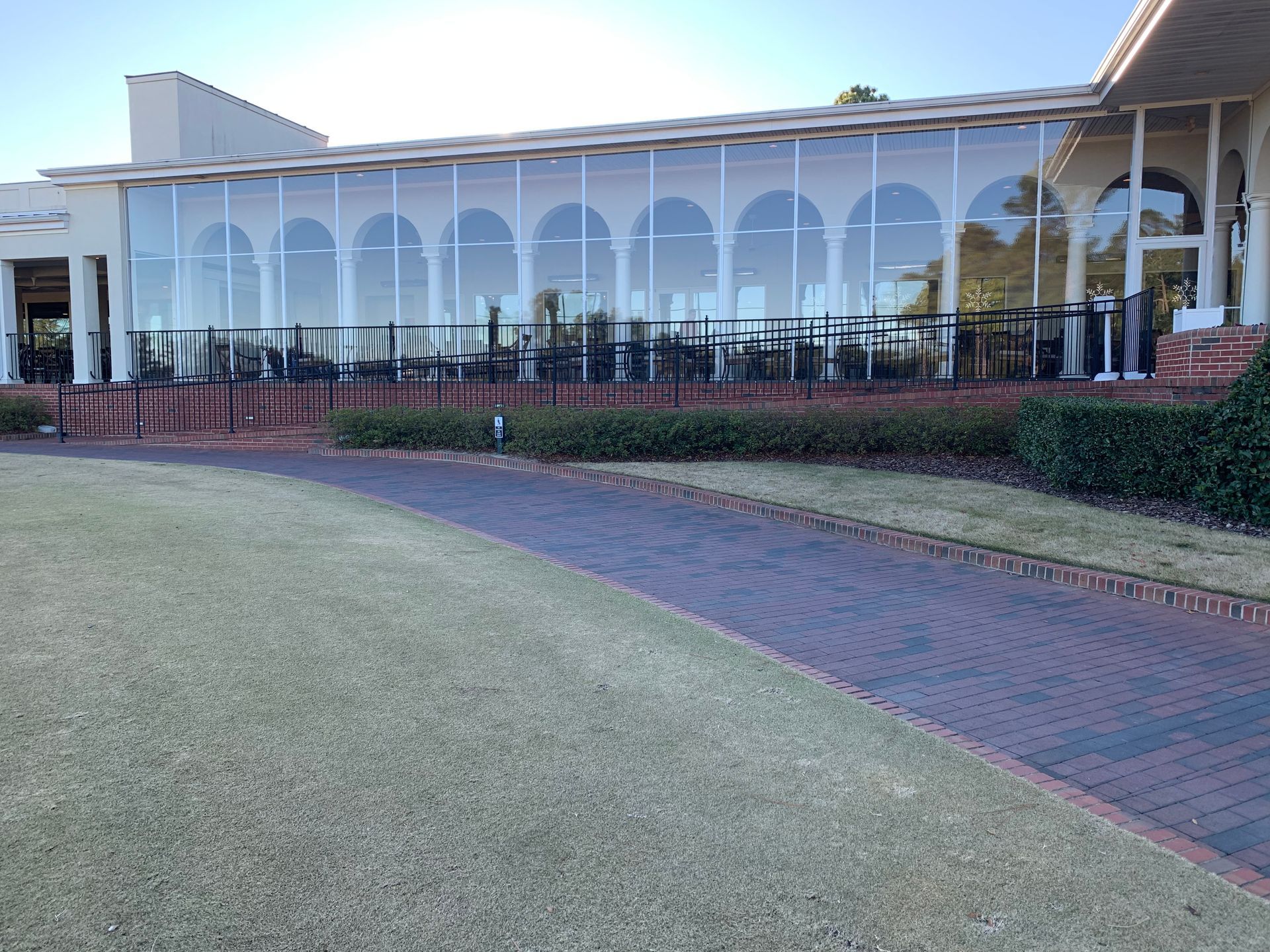White building with arched windows, brick walkway, and manicured lawn in front