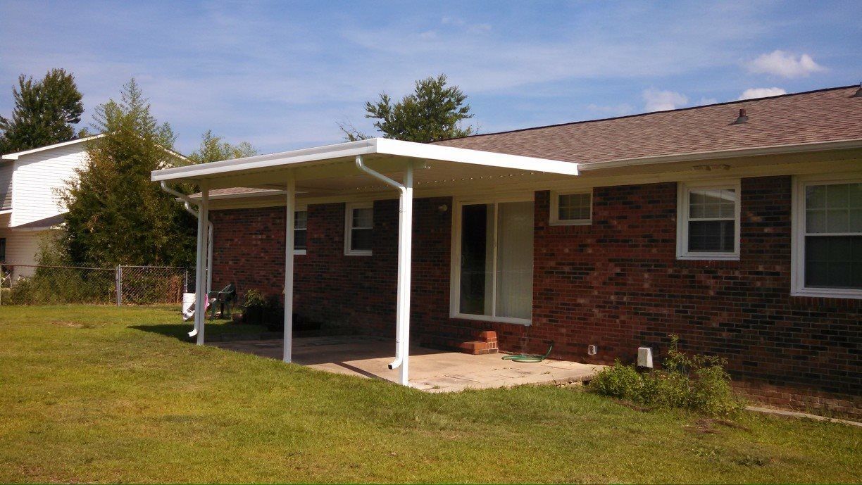 Brick house with a white carport and grassy front yard under a blue sky.