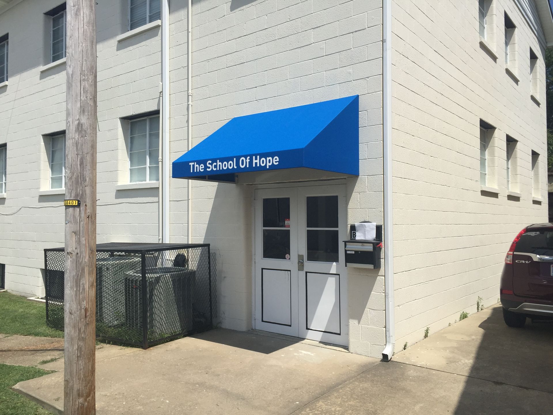 Blue awning over apartment entrance labeled “The School of Hope” on a beige building