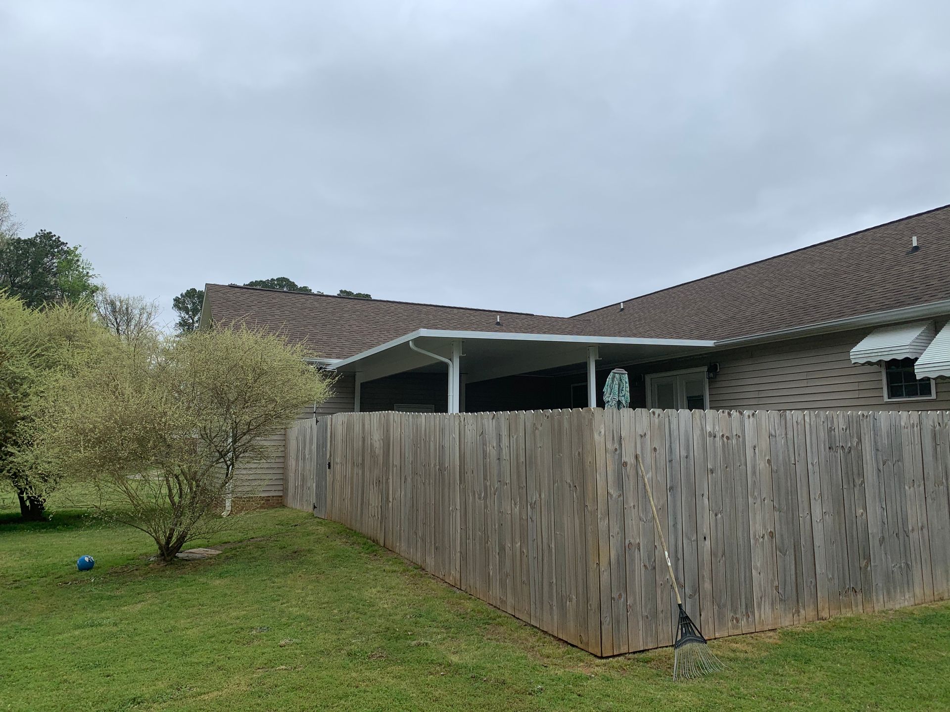 Backyard with wooden fence, grassy lawn, and house under a cloudy sky