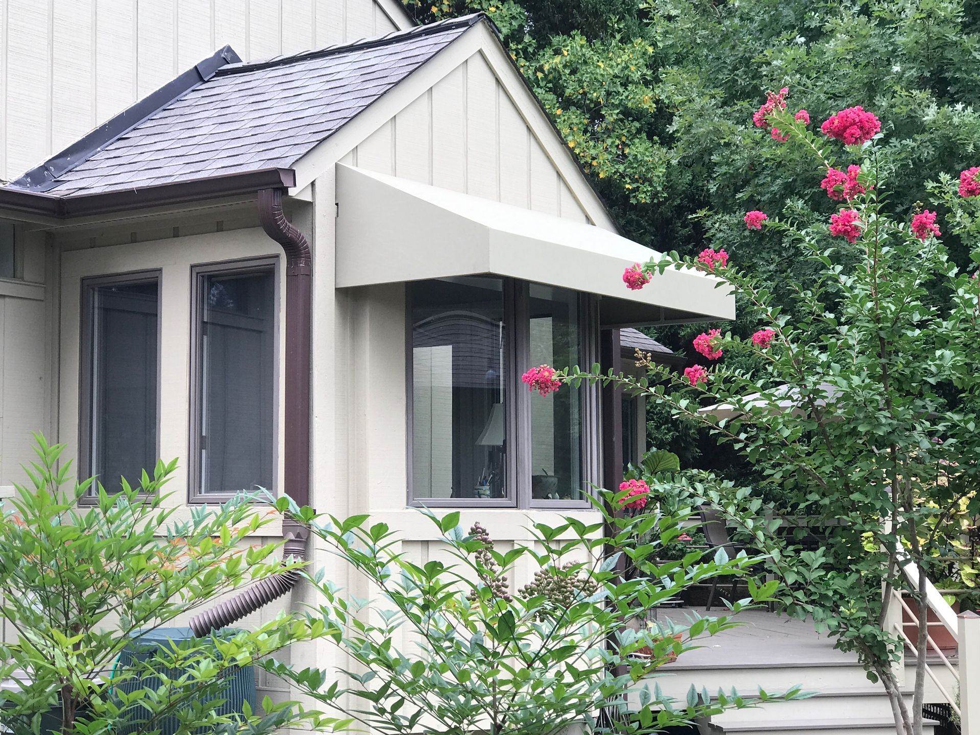 Small house with a white awning, surrounded by lush greenery and pink flowers