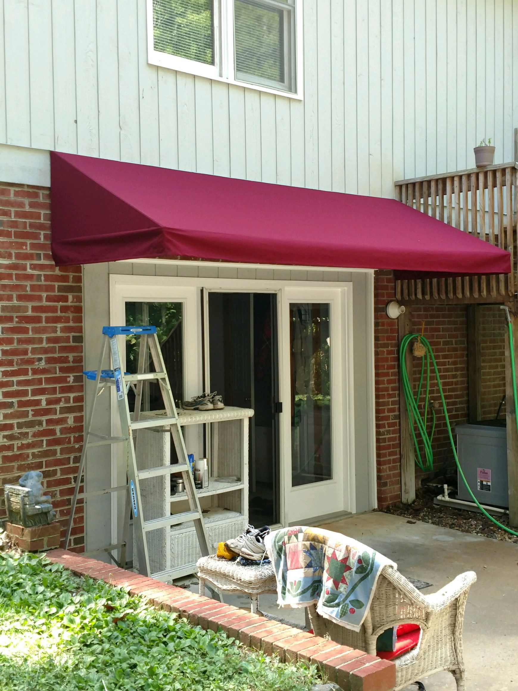 Back patio with maroon awning, white French doors, ladder, chairs, and garden hose by brick wall