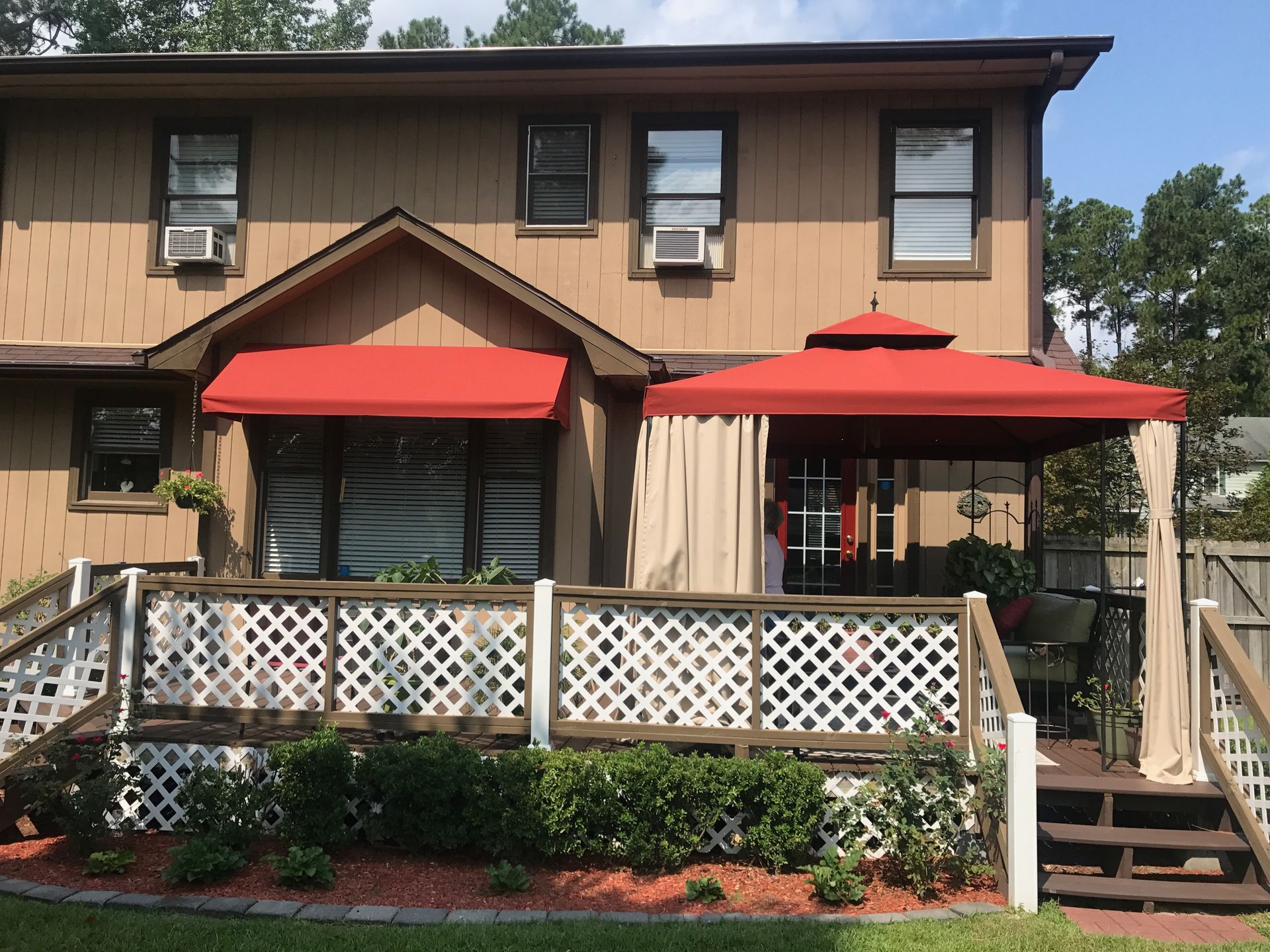 Two-story tan townhouse with red awnings and a white lattice porch railing