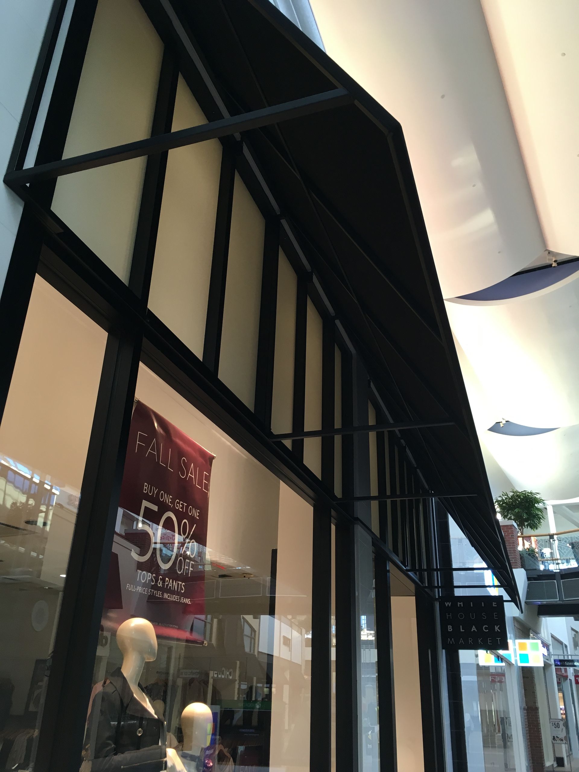 Storefront with black awning, glass windows, and a sale poster in a mall corridor